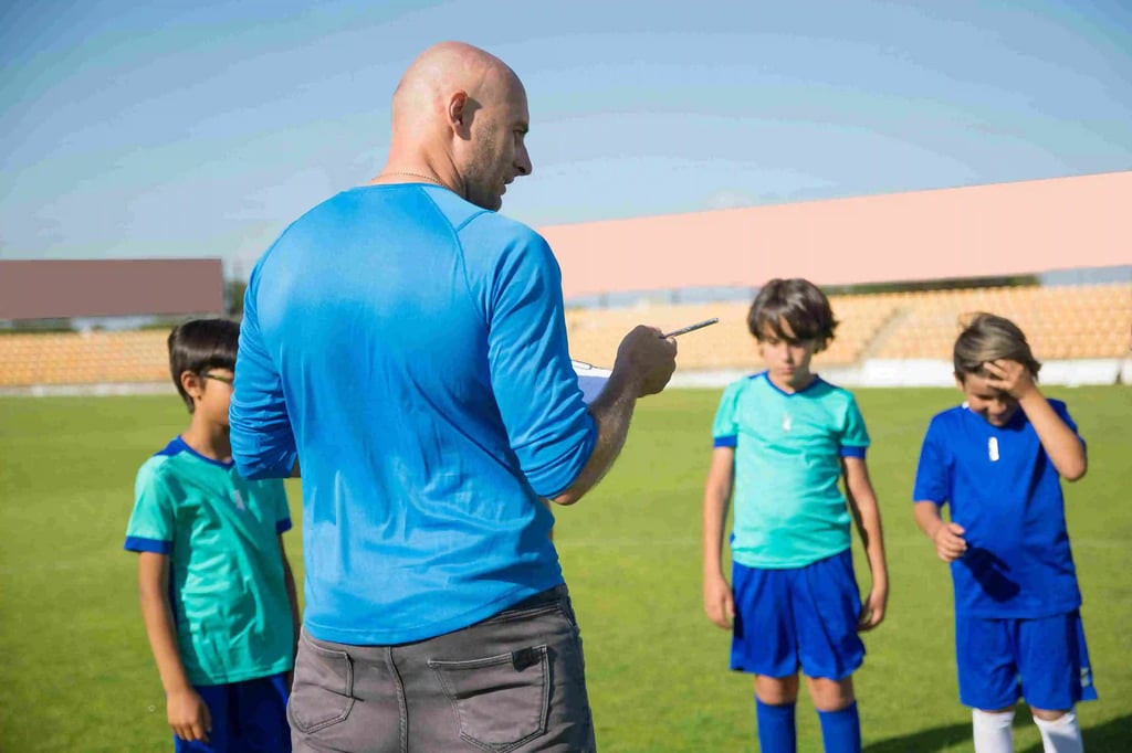  A man is talking with one younger boy in a dark blue shirt, who is giggling. Two other boys in turquoise shirts stand nearby. 